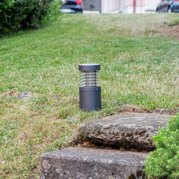 Moderne anthrazitfarbene Außenstandleuchte aus Metall auf einer Rasenfläche im Garten neben Natursteinstufen.