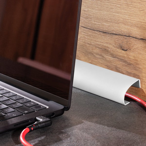 Ein silberner Kabelkanal auf einem Schreibtisch neben einem Laptop mit eingestecktem roten Kabel.