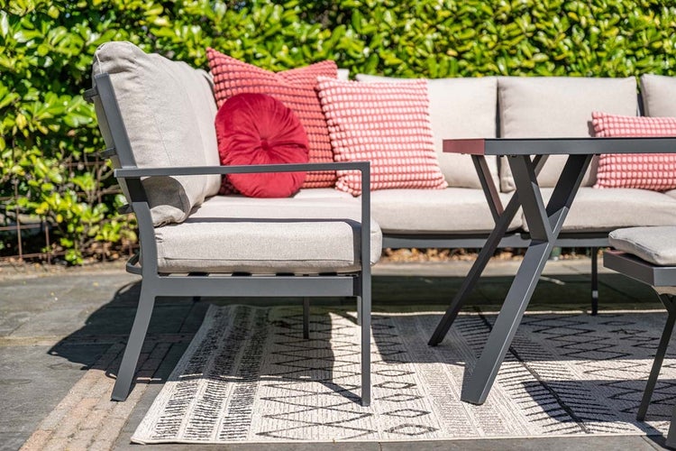 Modernes Garten-Lounge-Set aus anthrazitfarbenem Metall mit hellbeigen Polstern, roten Zierkissen und Tisch auf einem hellen Teppich im Freien.