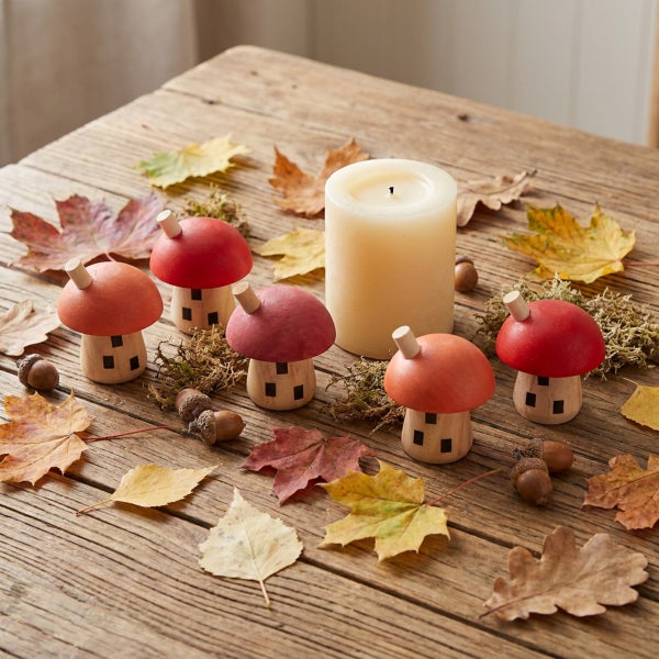 Herbstliche Tischdekoration mit Holzpilzfiguren, einer Stumpenkerze, Ahornblättern, Eicheln und Moos auf einem rustikalen Holztisch.