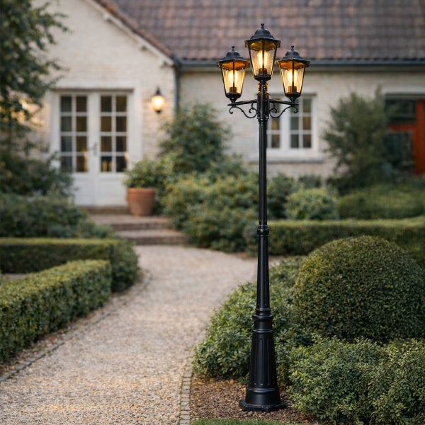 Dreiflammige Mastleuchte im klassischen Kandelaber-Stil an einem Kiesweg in einem Garten vor einem Haus.