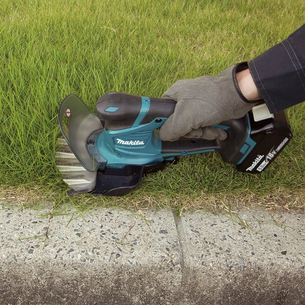 Makita Akku-Grasschere 18 Volt beim Schneiden einer Rasenkante an einem Weg aus Beton.