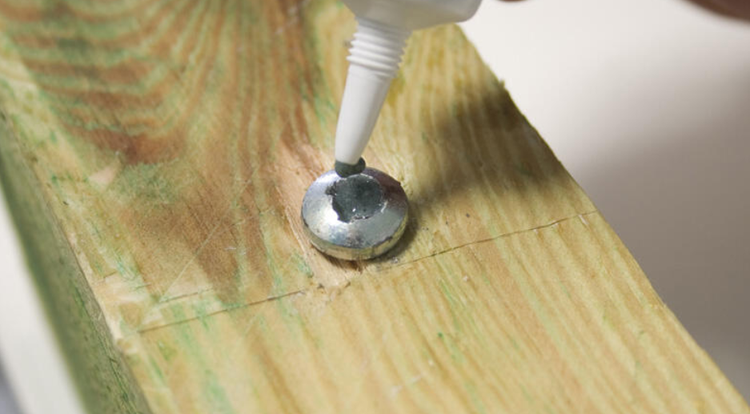 Holzbalken mit aufgeklebter Metallscheibe und Klebstofftube