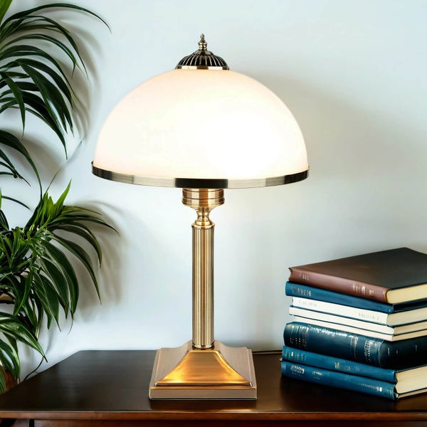 Tischleuchte mit Glasschirm neben einem Bücherstapel und einer Zimmerpflanze