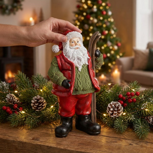 Weihnachtsfigur Weihnachtsmann mit Skiern als festliche Dekoration auf einem Tisch mit Tannenzweigen und verschwommenem Weihnachtsbaum im Hintergrund