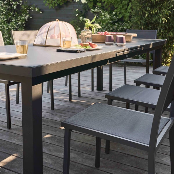 Modernes Gartenmöbel-Set aus einem großen rechteckigen Tisch und Stühlen mit Netzbespannung auf einer hellen Holzterrasse in einem Garten.