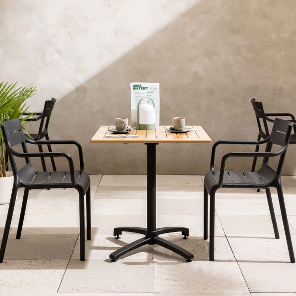 Modernes Bistro-Set mit hellem Holz-Lattentisch und schwarzen Kunststoff-Armlehnstühlen auf einer gefliesten Terrasse.