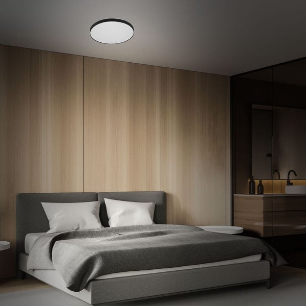 Runde LED-Deckenleuchte mit schwarzem Rahmen in einem modernen Schlafzimmer mit holzgetäfelten Wänden und grauem Polsterbett.