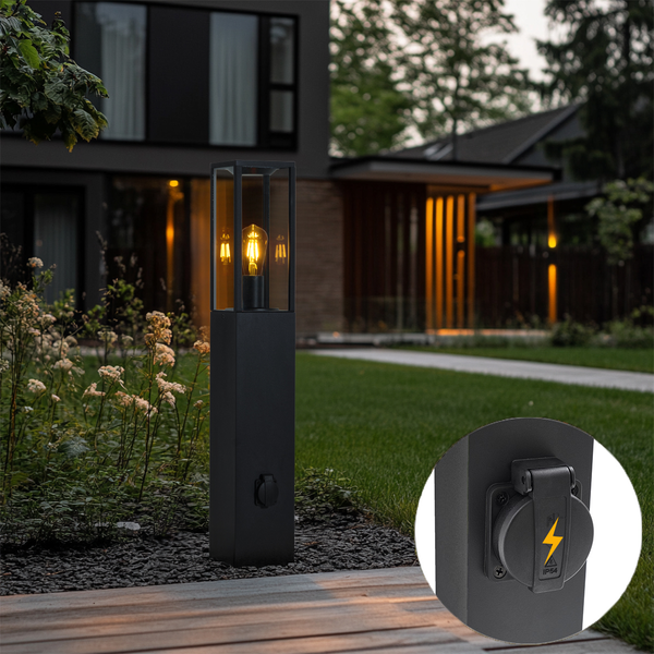 Moderne schwarze Außenstandleuchte mit Glaseinsatz und integrierter, geschützter Steckdose in einem Garten mit Rasen und Holzterrasse.