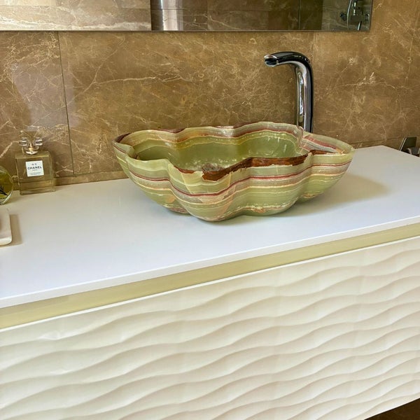 Helles Badezimmer mit einem Aufsatzwaschbecken aus Onyx mit wellenförmigem Rand auf einem Waschtischunterschrank mit Armatur vor einer Marmorwand.