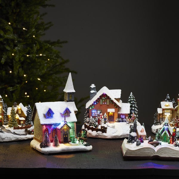 Weihnachtliche Miniaturdorf-Szene mit beleuchteten Häusern, Kirche und Tannenbäumen auf einer Oberfläche