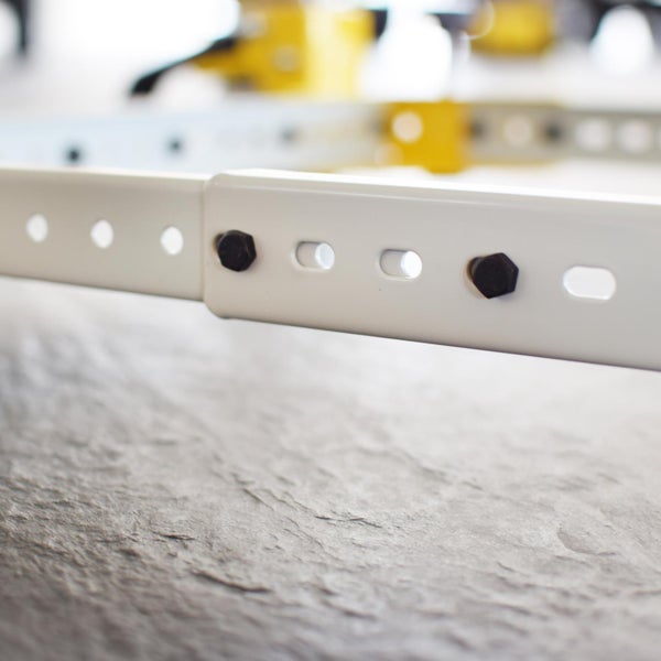 Detailaufnahme einer weißen Metallschiene mit Löchern und Schrauben