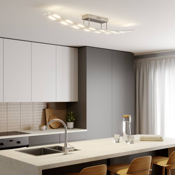 Moderne, geschwungene LED-Deckenleuchte in einer hellen, minimalistischen Küche mit Kochinsel, weißen Schränken und Holzstühlen.