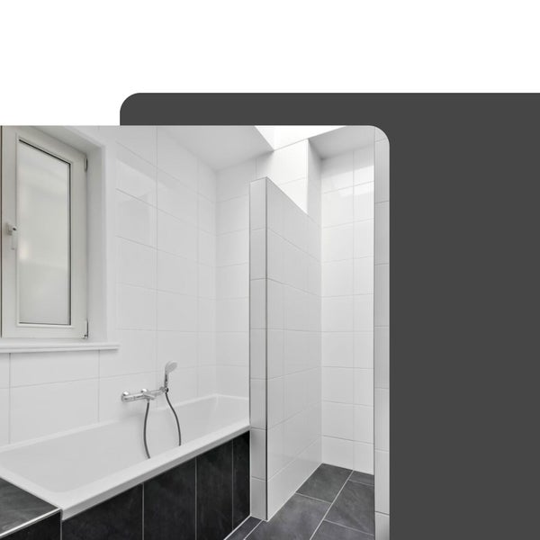 Helles Badezimmer mit weißer Einbaubadewanne, dunkler Verkleidung, weißen Wandfliesen und einer Dusche mit Trennwand.
