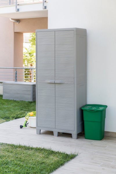 Grauer Gartenschrank aus Kunststoff mit zwei Türen und einem grünen Mülleimer im Garten