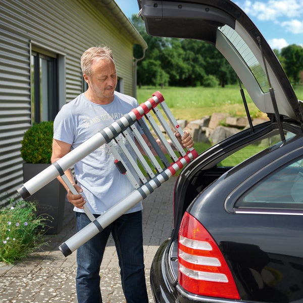 Mann verstaut eine Teleskopleiter im Kofferraum eines Autos.