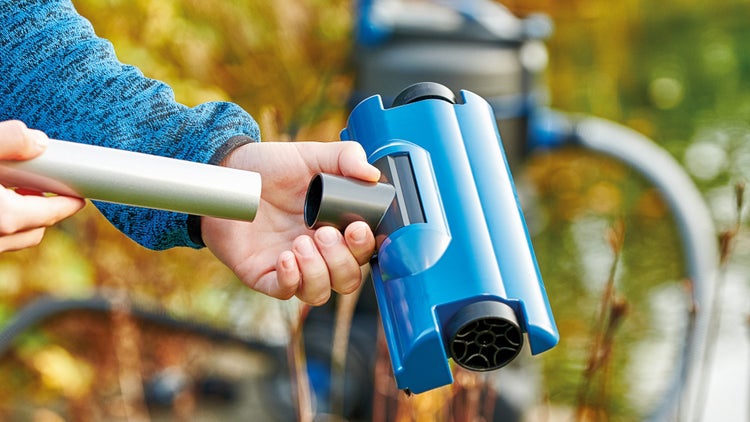 Eine Person verbindet einen blauen Teichreiniger-Aufsatz mit einer silbernen Aluminium-Teleskopstange zur Teichpflege.