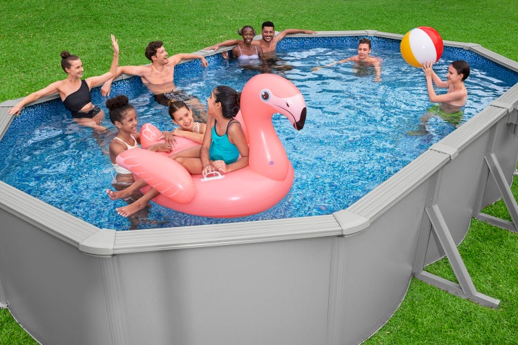 Ovaler Aufstellpool mit grauer Außenwand und blau gemusterter Folie, in dem Erwachsene und Kinder mit einem Flamingo-Schwimmtier und Ball spielen.