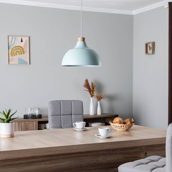 Moderne hellblaue Pendelleuchte mit Holzdetail über einem hölzernen Esstisch in einem hellen, aufgeräumten Esszimmer.