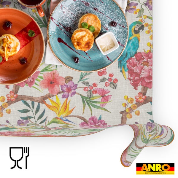 Abwaschbare Tischdecke mit tropischem Blumenmuster und Papagei, gedeckt mit Tellern und Speisen, lebensmittelecht, ANRO Logo.