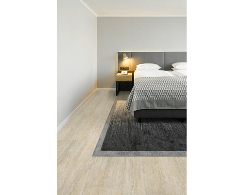 Modernes Schlafzimmer mit hellem Boden in Steinoptik, grauem Bett, Teppich und Nachtischlampe in einem hellen, aufgeräumten Raum.