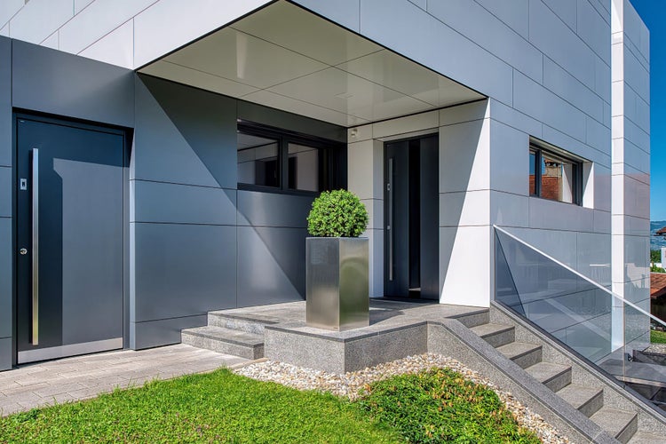 Moderner Hauseingang mit grauer Haustür, Steintreppe und einer Fassadenverkleidung aus großformatigen Platten.