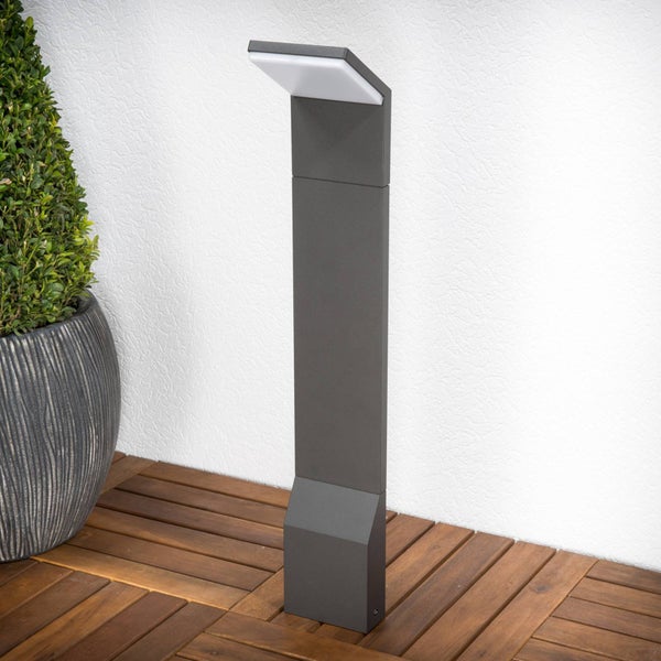 Moderne LED-Pollerleuchte aus anthrazitfarbenem Metall auf Holzterrasse. Die Außenleuchte hat ein minimalistisches Design mit geneigtem Kopf.