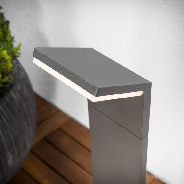 Moderne LED-Wegeleuchte in Anthrazit auf einer Holzterrasse neben einem Pflanzgefäß.