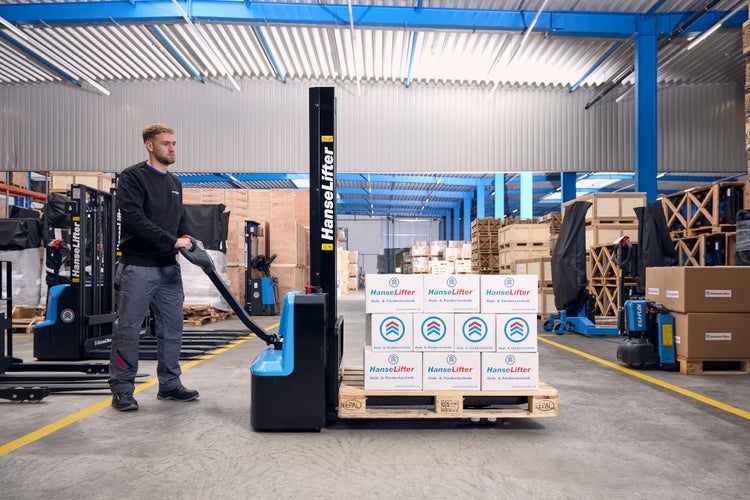 Mitarbeiter bedient elektrischen Deichselstapler von HanseLifter in einer organisierten Lagerhalle, beladen mit Kartons auf einer Europalette.