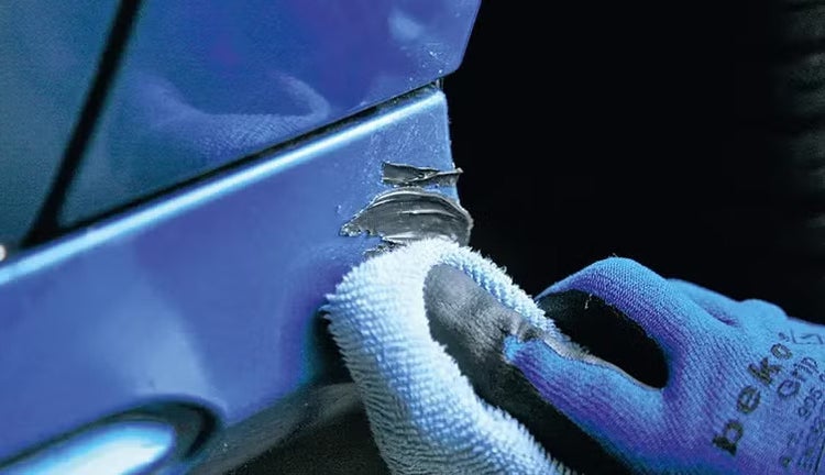 Anwendung von Reparaturmasse auf einer Autostoßstange mit einem Mikrofasertuch und einem Arbeitshandschuh mit beko Logo.