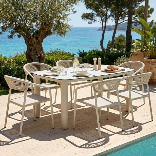 Modernes Gartenmöbel-Set mit rechteckigem Esstisch und sechs Stühlen mit Seilgeflecht auf einer hellen Terrasse am Pool mit Meerblick.