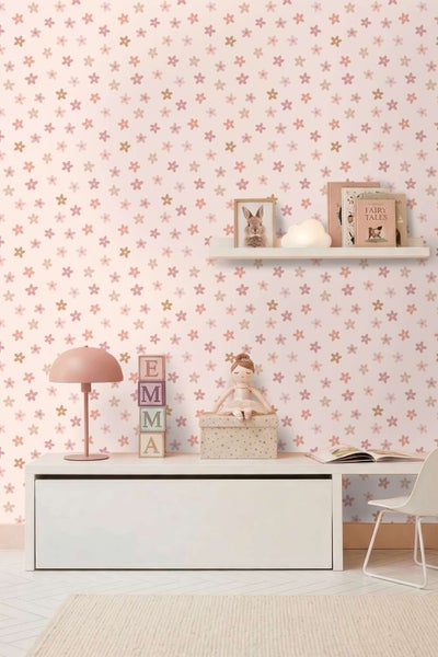 Kinderzimmer mit Tapete mit Blumenmuster, weißem Sideboard, Tischlampe, Spielzeug und Wandregal mit Bilderrahmen und Büchern.