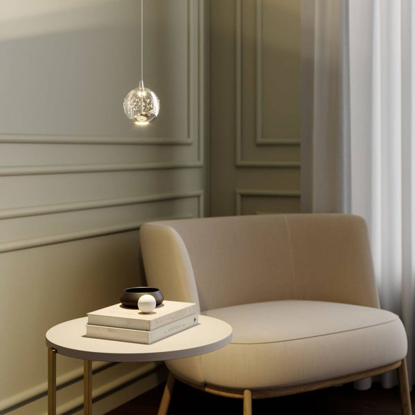 Hängeleuchte mit funkelnder Glaskugel in einem hellen, modern eingerichteten Raum mit Sessel und rundem Beistelltisch.