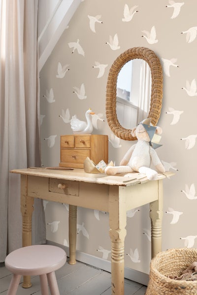 Dekoratives Kinderzimmer mit Spiegel, Tisch, Hocker und Accessoires vor einer Tapete mit Schwanenmotiv