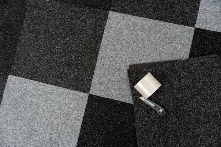 Verlegen von Teppichfliesen im Schachbrettmuster mit einem Cuttermesser und doppelseitigem Klebeband.