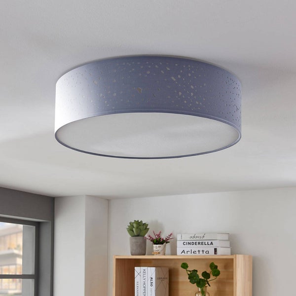 Helle, organisierte Szene mit einer runden Deckenleuchte aus blau-grauem Stoff mit Sternenhimmel-Effekt über einem Holzregal mit Büchern und Pflanzen.