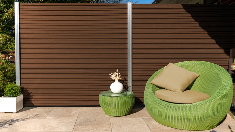 Terrasse mit braunem Sichtschutzzaun, grünem Korbsessel, Beistelltisch und dekorativer Bepflanzung