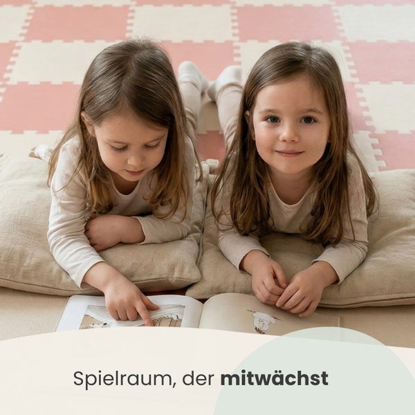 Zwei Kinder liegen auf Kissen auf einer weichen Spielmatte aus Schaumstoff in einem hellen Spielzimmer und lesen ein Buch.