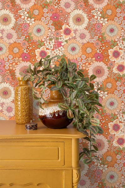 Wohnraumgestaltung mit Vliestapete mit Blumenmuster vor einer Kommode mit dekorativen Vasen und einer Kunstpflanze.