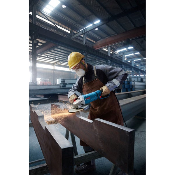 Ein Arbeiter mit Schutzkleidung schleift Metall mit einem Winkelschleifer in einer Fabrikhalle.