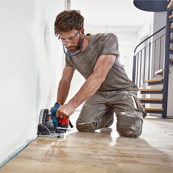 Handwerker beim Schneiden von Holz mit einer Tauchsäge auf einem Holzboden.