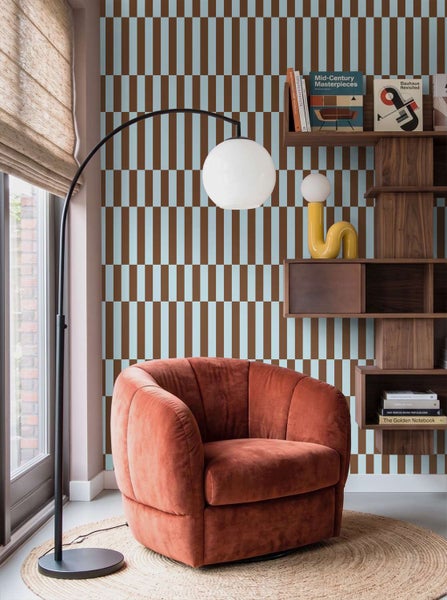 Wohnraum mit gemusterter Tapete, einem samtigen Sessel, einer Bogenlampe und einem Holzregal im Mid Century Stil.