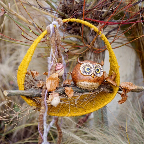 Dekorative hängende Eule aus Keramik im Nest aus Ästen und Garn zur herbstlichen Gartendekoration
