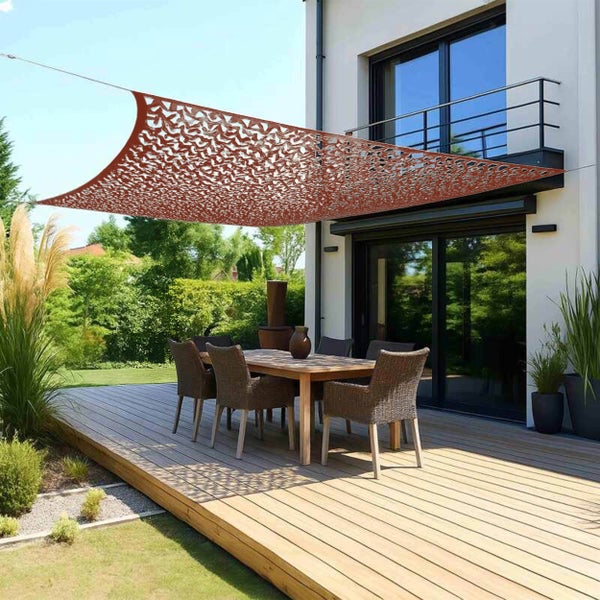 Sonnensegel im Tarnnetz-Design über einer Terrasse mit Gartenmöbeln auf einem Holzdeck, umgeben von einer Hecke, Pflanzen und einem Gartenhaus.