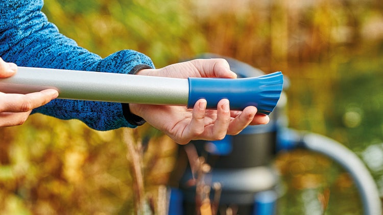 Montage einer blauen Kunststoffdüse an ein silbernes Aluminium-Saugrohr eines Teichsaugers im Gartenbereich.