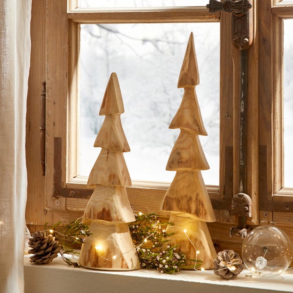 Dekorative Holzweihnachtsbäume auf einer Fensterbank mit Tannenzapfen und Lichterkette.