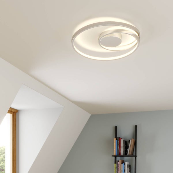 Moderne LED-Deckenleuchte mit mehreren Leuchtringen an einer weißen Decke in einem hellen Raum mit Bücherregal.