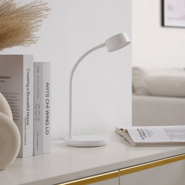 Weiße LED-Schreibtischlampe mit flexiblem Hals auf einem Tisch neben Büchern und einer Zeitschrift.