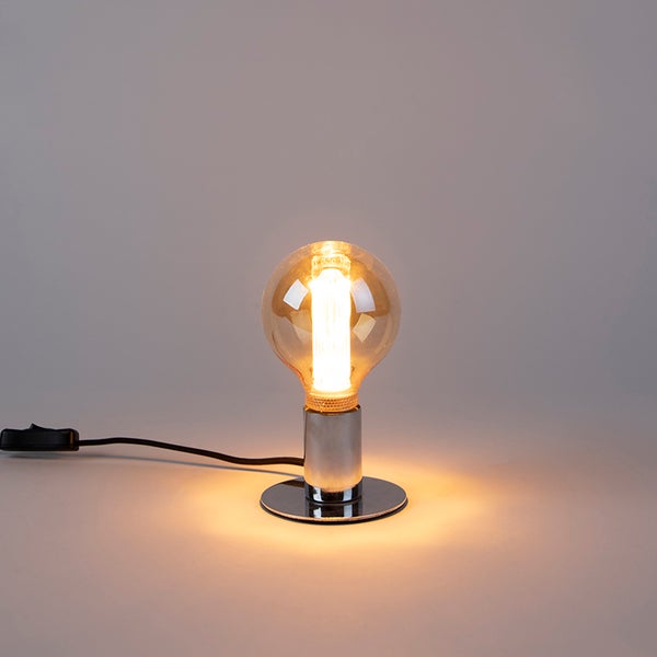 Eingeschaltete Tischleuchte mit verchromtem Sockel und kugelförmigem Glasleuchtmittel.