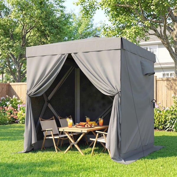 Grauer Gartenpavillon mit gerafften Vorhängen im Garten, ausgestattet mit einer hölzernen Sitzgruppe bestehend aus Klapptisch und Klappstühlen.